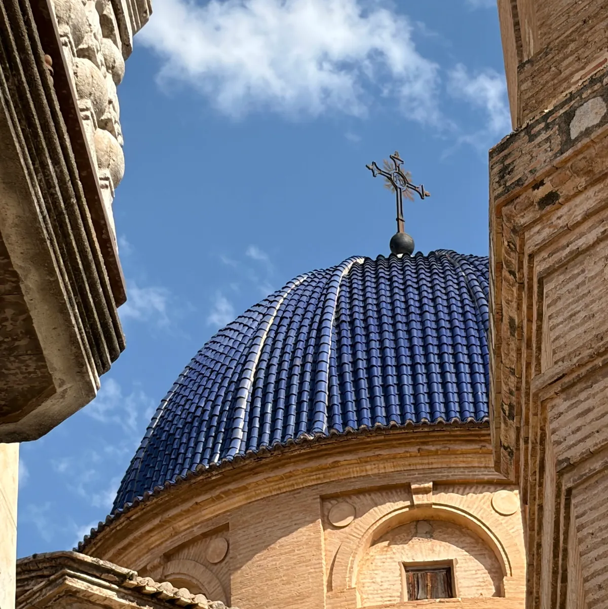Close-up of a blue-tiled church dome with a cross, framed by stone archways in Xaló